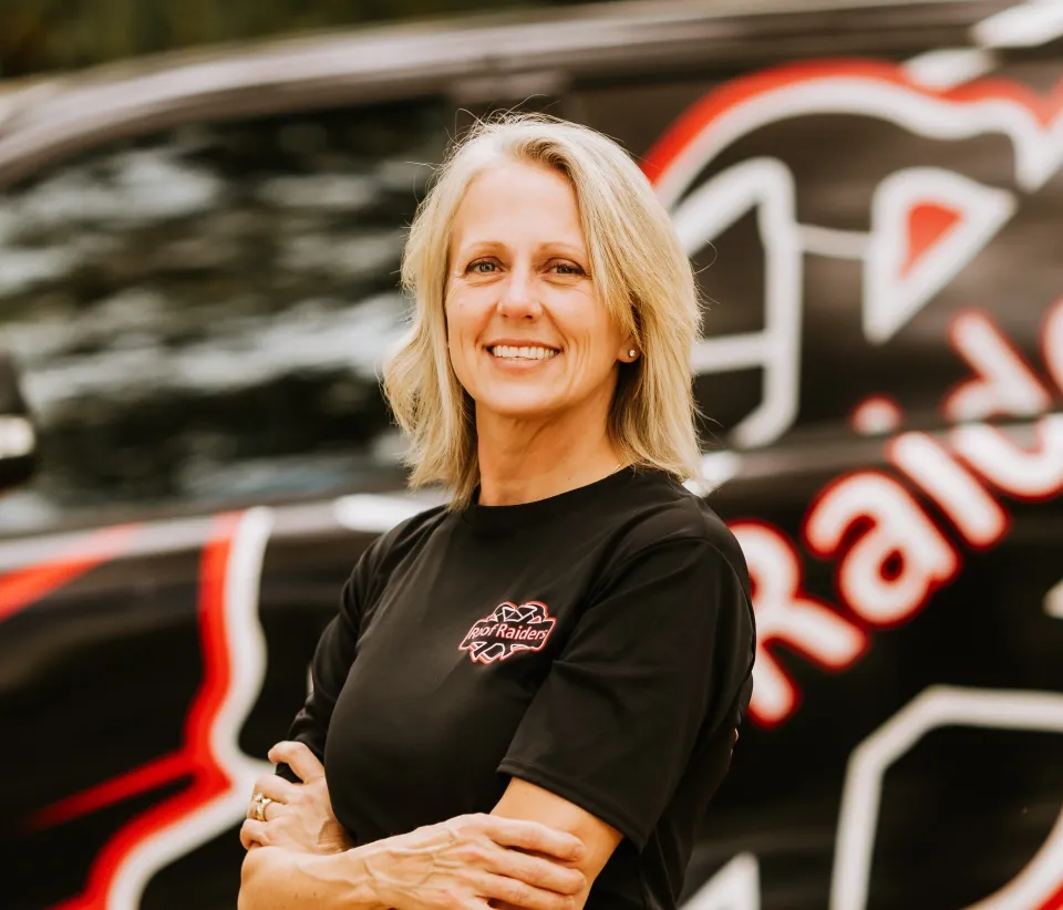 Tammy Martin standing in front of a Roof Raiders truck smiling with her arms crossed.