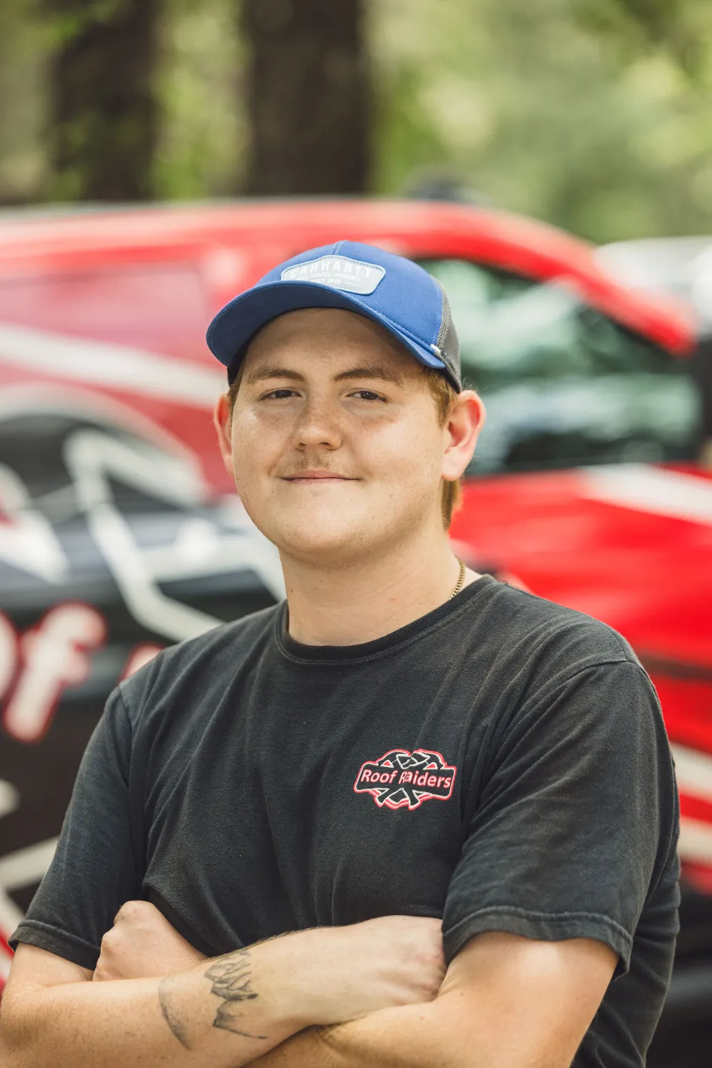 Jarrett Earnest smiling with his arms crossed in front of a Roof Raiders truck.