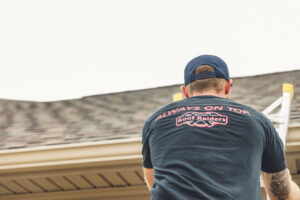 A man in a black Roof Raiders shirt climbing a ladder to a roof.